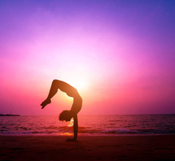 Piękna młoda kobieta practic jogi na plaży. Wczesnym rankiem wykonywania. Wschód słońca. Tle palmy - Zdjęcie, obraz