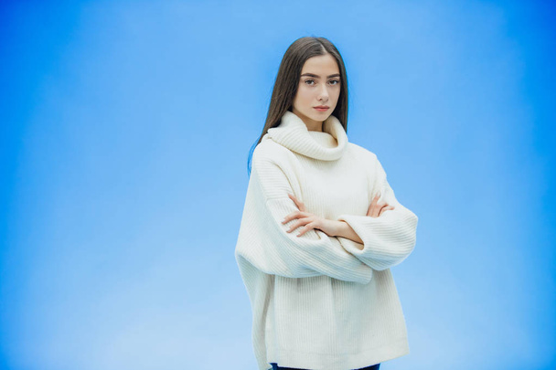 Girl in a white sweater on a blue background. Put your hand on your arm. The concept of hope for the opening of a new work - Fotoğraf, Görsel