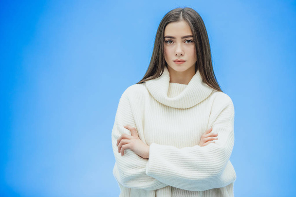 The image of a happy young lady standing on a blue background. Look to the side. During this time she is dressed in a white warm sweater. - Foto, Bild