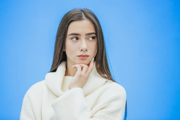The image of a happy young lady standing on a blue background. Look to the side. During this time she is dressed in a white warm sweater. - Photo, Image