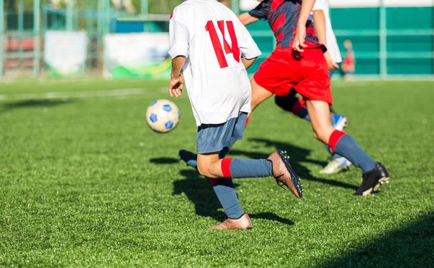少年サッカーのフィールドで実行している赤白のスポーツウェア。若い選手はドリブルし、ゲームでサッカー ボールを蹴る。トレーニング、アクティブなライフ スタイル、スポーツ、子供の活動の概念  - 写真・画像