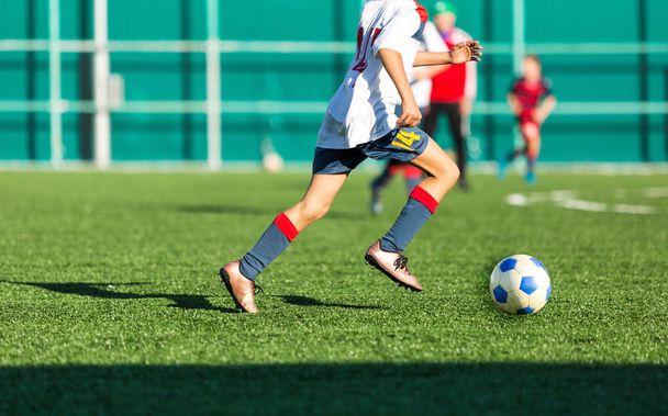 Αγόρια κόκκινο λευκό sportswear τρέχει στο γήπεδο ποδοσφαίρου. Νέους ποδοσφαιριστές ντρίμπλα και κλωτσήσει μπάλα ποδοσφαίρου στο παιχνίδι. Κατάρτισης, ενεργό τρόπο ζωής, αθλητισμό, έννοια δραστηριότητα τα παιδιά  - Φωτογραφία, εικόνα