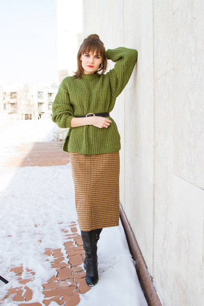 Beautiful young girl in a green sweater, leaning against a wall - Photo, Image