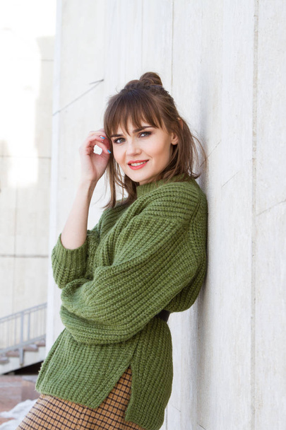 Beautiful young girl in a green sweater, leaning against a wall - Φωτογραφία, εικόνα