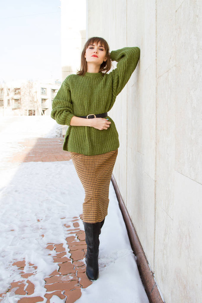 Beautiful young girl in a green sweater, leaning against a wall - Photo, Image