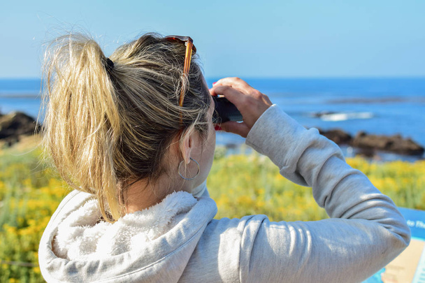 Young woman looking through binoculars at the seaside - Fotoğraf, Görsel