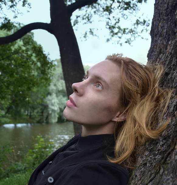 πορτρέτο ενός νεαρού άνδρα, με μακριά ξανθά μαλλιά που αναπαύεται στο πάρκο - Φωτογραφία, εικόνα