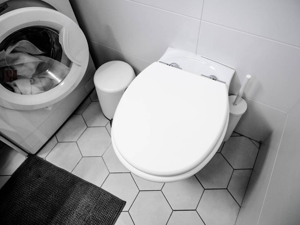 Toilettes blanches modernes avec quelques chiffons dans une machine à laver, sol carrelage
. - Photo, image