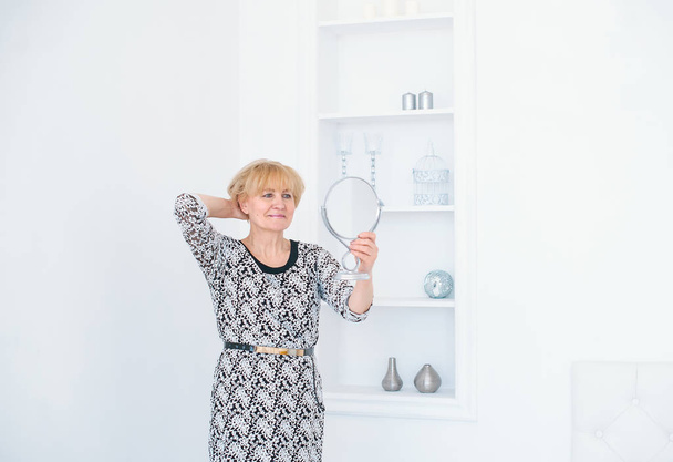 Gyönyörű magas rangú nő gazdaság tükör kézzel a fehér stúdió - Fotó, kép