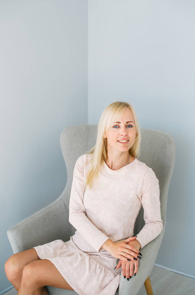 Belle fille blonde assise sur un fauteuil dans un studio bleu clair
 - Photo, image