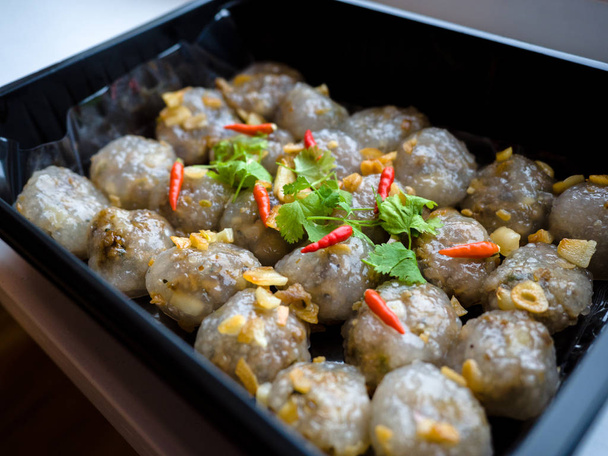 thailändische Vorspeise, gedämpfte Tapiokabällchen mit Erdnuss- und Schweinefleischfüllung mit Chili, Koriander und Knoblauch in einer schwarzen Plastiktablett-Box zum Mitnehmen. - Foto, Bild