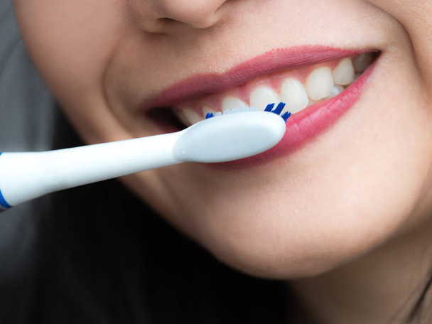 Fast moving electronic toothbrush and cleaning mouth, Smiling healthy pretty woman using a generic white electric toothbrush to brush her teeth in an oral hygiene, healthcare and dentistry concept. - Fotó, kép