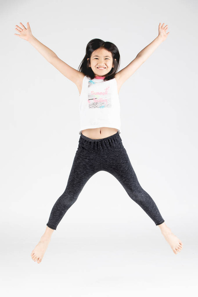Ázsiai vicces gyermek lány jumping szürke háttér. - Fotó, kép