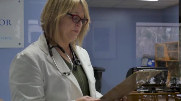 Médecin femme examinant les dossiers sur un presse-papiers dans une pratique médicale moderne
 - Séquence, vidéo