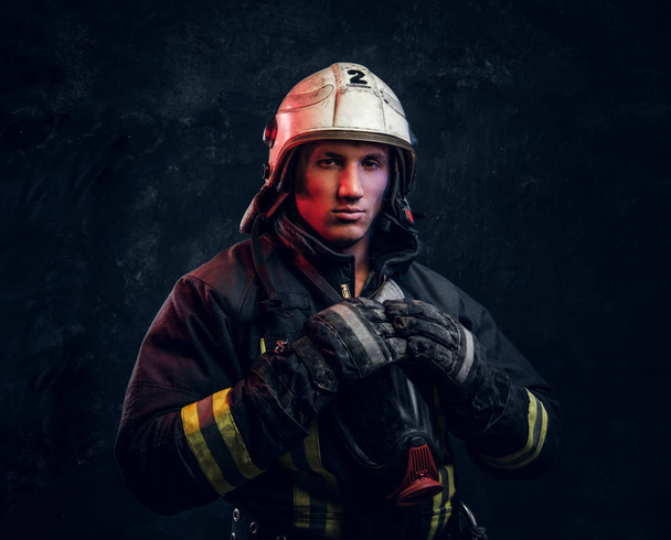 Пожарный в форме и шлеме безопасности позирует в темной студии
 - Фото, изображение