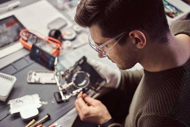 der Techniker repariert ein beschädigtes Smartphone in der Elektronikwerkstatt. - Foto, Bild