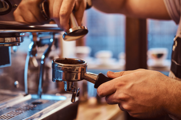 Γκρο πλαν φωτογραφία από ένα χέρι που κρατά ένα portafilter με ένα μαύρο αλεσμένος καφές σε ένα κατάστημα καφέ ή εστιατόριο - Φωτογραφία, εικόνα