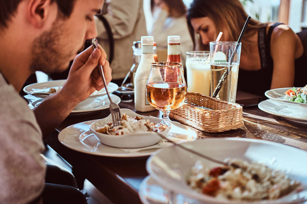 Immagine ravvicinata di un giovane uomo con i suoi amici che mangia un'insalata fresca e sana in un caffè all'aperto durante la pausa pranzo
 - Foto, immagini
