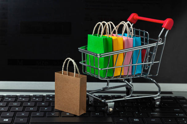 Nákup zboží a oblečení v internetovém obchodě. Nákupní tašky do nákupního košíku na klávesnici pro laptop - Fotografie, Obrázek