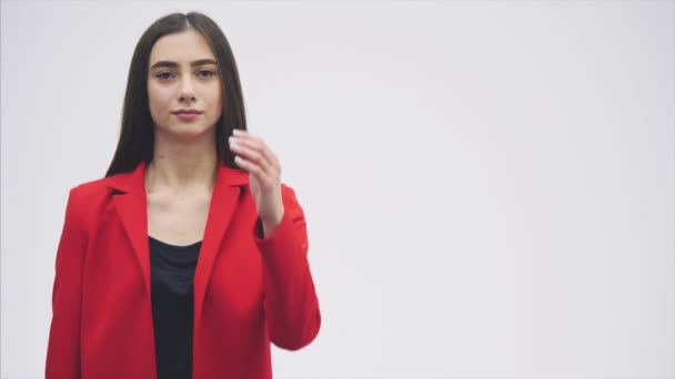Portrait of a beautiful young brunette. Look into the camera. During this she raised her hand and began to show a gesture of greetings. Dressed in a red jacket. - Video, Çekim
