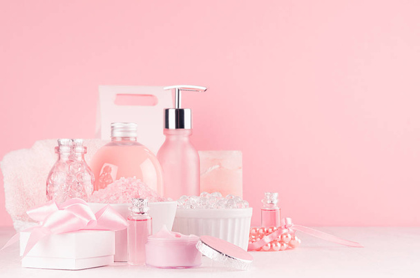 Gentle girlish dressing table with cosmetics products - rose oil, bath salt, cream, perfume, cotton towel, bottle, bowl, box in white, pastel pink interior. - Foto, Bild