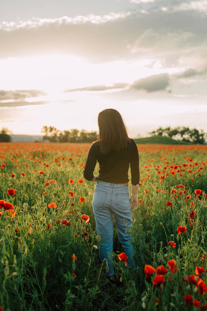 meisje staat met haar rug in het veld met bloemen. zomeravond. Ruimte voor tekst kopiëren - Foto, afbeelding