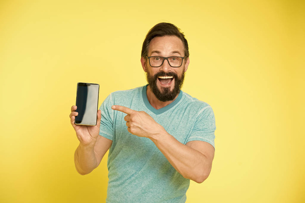 Check out new app. Guy eyeglasses cheerful pointing at smartphone. Man happy user recommends try application for smartphone. Man takes advantages online communication. Guy bearded smartphone user - Foto, imagen