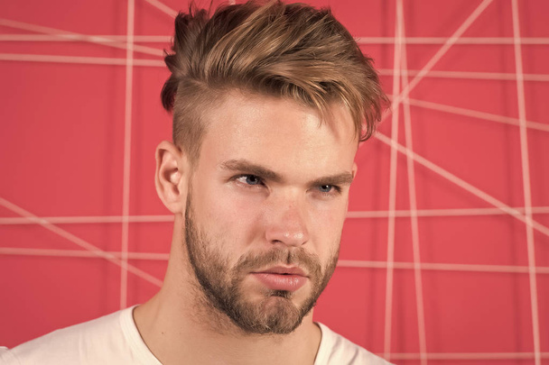 Man with bristle on strict concentrated face, pink background. Masculinity concept. Guy bearded and attractive with hairstyle. Man with beard or unshaven guy looks handsome and well groomed - Photo, image