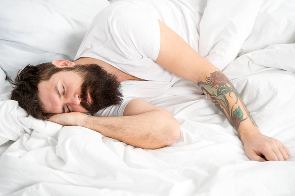 Lazy morning. Man bearded hipster sleepy in bed. Early morning hours. Insomnia and sleep problems. Relax and sleep concept. Man bearded guy sleep on white sheets. Healthy sleep and wellbeing - Fotografie, Obrázek