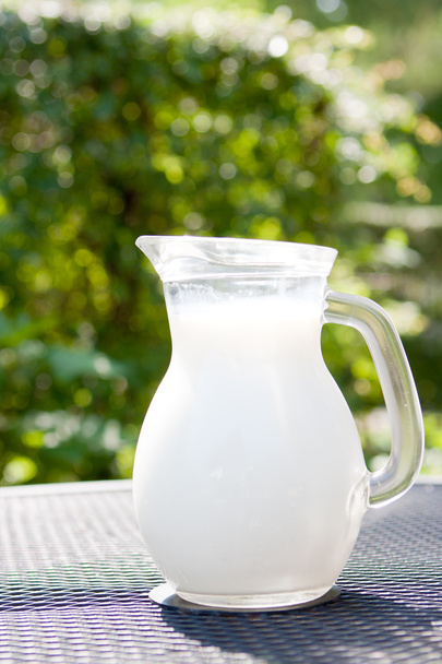 verse melk in glazen kan op een tafel - Foto, afbeelding
