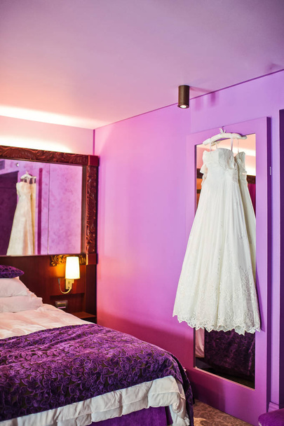 Біла сукня нареченої в інтер'єрі готелю, фіолетовий фон
 - Фото, зображення