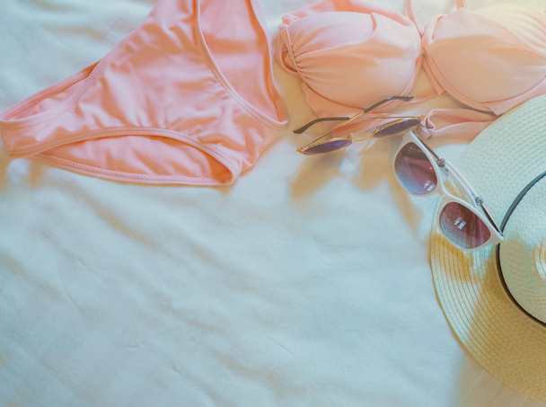 Çarşaf üzerinde üstten görünüm bikini mayo, güneş gözlüğü ve hasır şapka. Kadının mayo ve plaj aksesuarları resort yatak üzerinde. Pembe bikini mayo plaj için ayarla. Yaz tatili ve yaz vibes. - Fotoğraf, Görsel