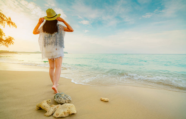 Une jeune femme heureuse porte un chapeau de paille marchant sur la plage. Détendez-vous et profitez de vacances sur la plage paradisiaque tropicale avec de l'eau de mer verte émeraude. Fille en vacances d'été. Des vibrations estivales. Coraux morts sur la plage
.  - Photo, image