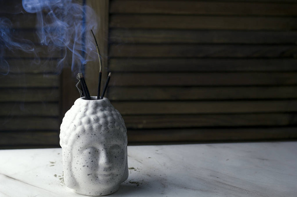 Boeddha hoofd met bloem, wierook stokje op een houten achtergrond - Foto, afbeelding