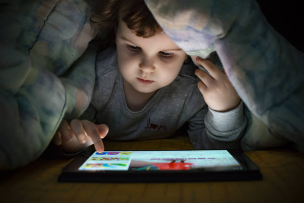 Little girl watching her tablet in the bed. Illuminated child fa - Photo, Image