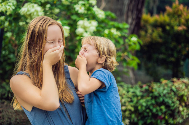 Mother and son blowing nose in front of blooming tree. Spring allergy concept. Childrens allergies - Fotoğraf, Görsel
