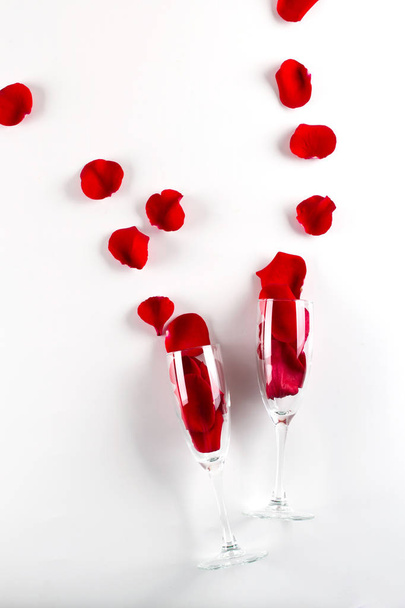 Two glasses with rose petals on white background.Celebration concept. Top view, copy space for text - Foto, Imagem