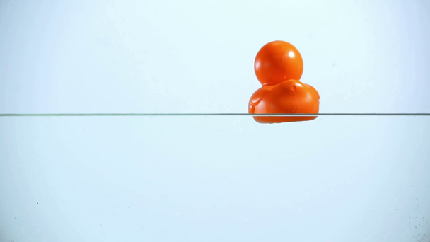 Nézd, az ember nyomja a narancssárga gumi kacsa a víz a kék háttér megvilágítású vágott - Felvétel, videó