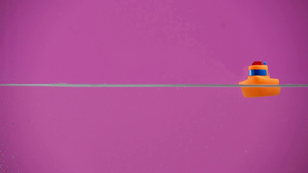 oříznutý pohled člověka tlačí oranžové gumový člun na vodě na fialovém pozadí - Záběry, video