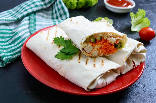 Delicious shawarma sandwich on a black background. Burritos wraps with grilled chicken and vegetables, greens. Fajitas, pita bread. Traditional Middle Eastern appetizer. Mexican cuisine - Photo, Image
