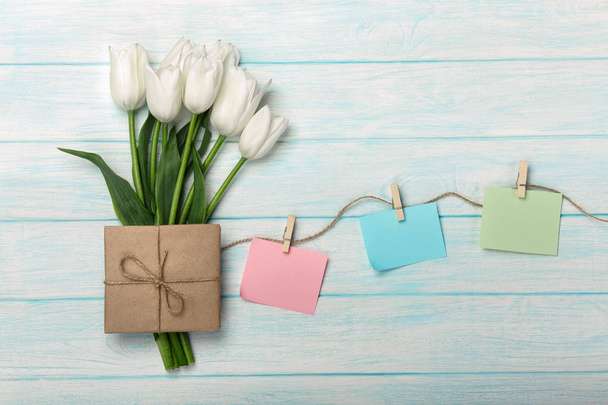 Букет белых тюльпанов и конверт с цветными наклейками с прищепками на веревке и синими деревянными досками
 - Фото, изображение