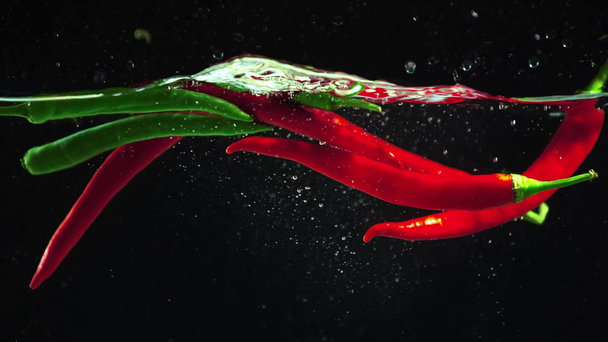 Studio-Shooting von bunten grünen und roten Paprika, die in klares Wasser auf schwarzem Hintergrund tauchen - Filmmaterial, Video