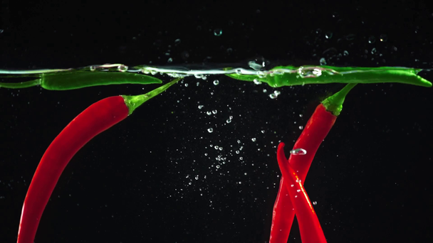 sesión de estudio de coloridos chiles verdes y rojos que caen con salpicaduras en el agua clara sobre fondo negro
 - Imágenes, Vídeo