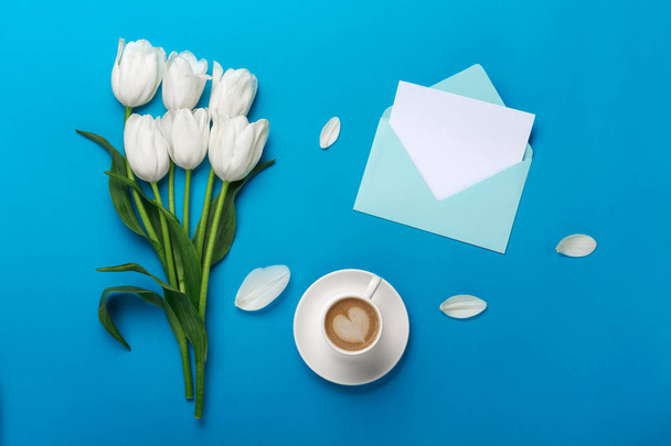 Белые тюльпаны с лепестками, чашка кофе, любовная записка и цветной конверт на синем фоне
 - Фото, изображение