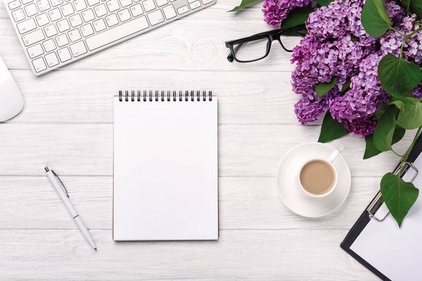Schreibtisch im Büro mit Fliederstrauß, Kaffeetasse, Tastatur, Notizbuch und Stift auf weißen Tafeln - Foto, Bild