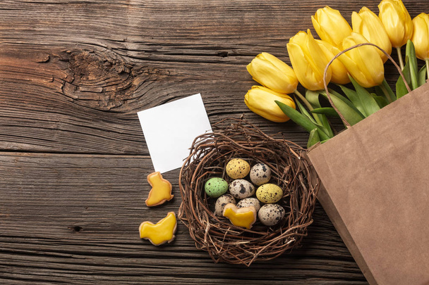 Easter gingerbread cookies on wooden table and yellow tulips. Greeting card. Top view with copy space. - Photo, Image