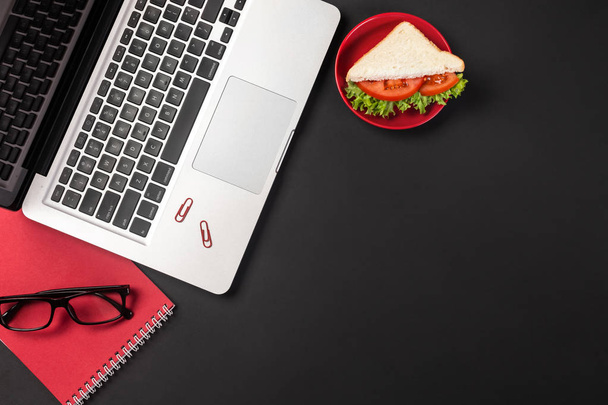 Elegante desktop per ufficio nero con laptop, tazza di caffè e un panino per il pranzo. Vista dall'alto con spazio di copia
. - Foto, immagini