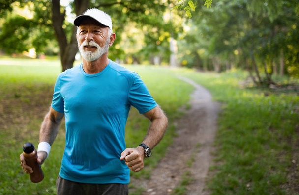 Attractive retired senior man with a nice smile jogging in park - Photo, image