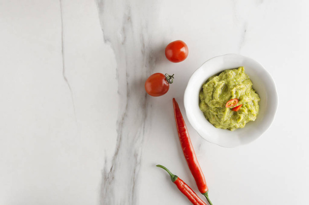 Bovenaanzicht van kom met lekkere guacamole met Chili peper en tomaten geserveerd op witte tafel in de keuken, lege ruimte - Foto, afbeelding