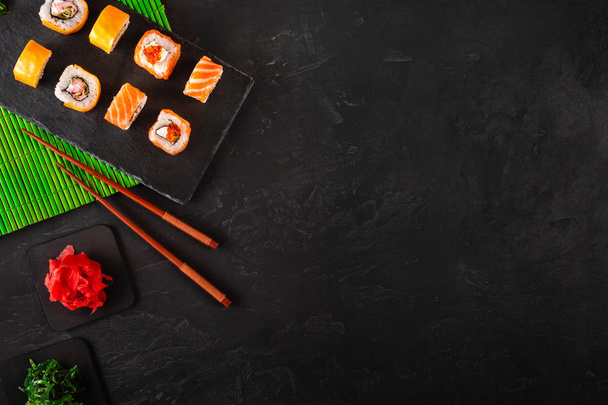 Palillos de sushi japoneses sobre un tazón de salsa de soja, arroz sobre fondo de piedra negra. Vista superior con espacio de copia
 - Foto, Imagen